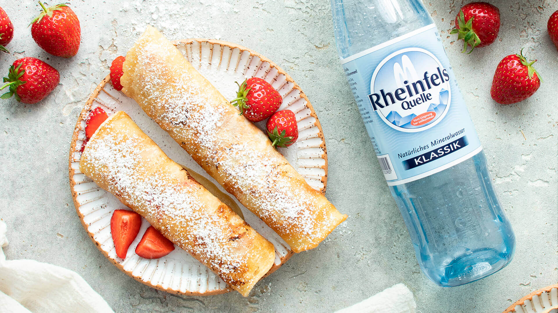 Pfannkuchen mit frischen Erdbeeren und eine Flasche Rheinfels Quelle Klassik.