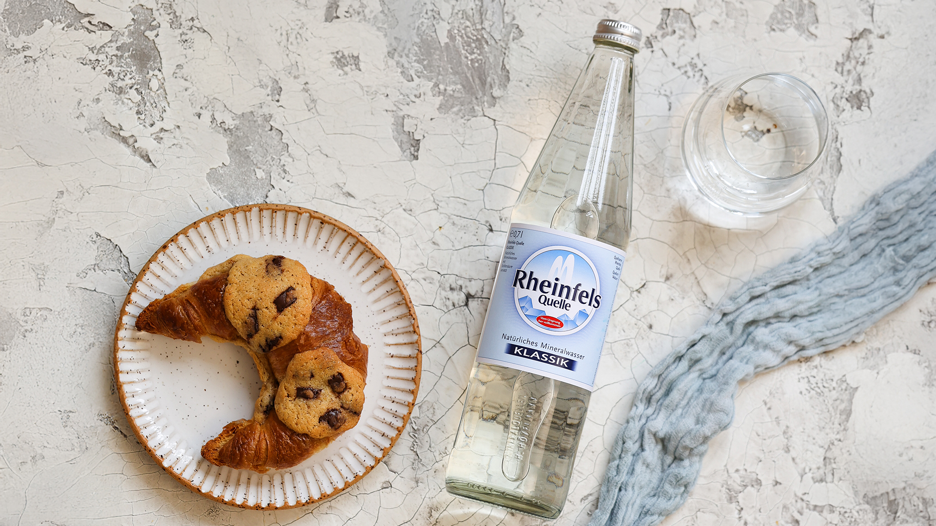 Crookies auf einem Teller liegend. Der Teller steht auf einem Tisch, daneben eine Flasche Rheinfels Quelle Klassik 0,7 L Glas Mehrweg.