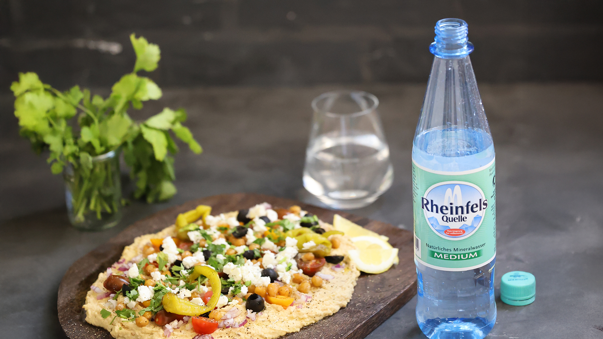 Mediterranes Hummusboard daneben steht ein Flasche Rheinfels Quelle Medium.