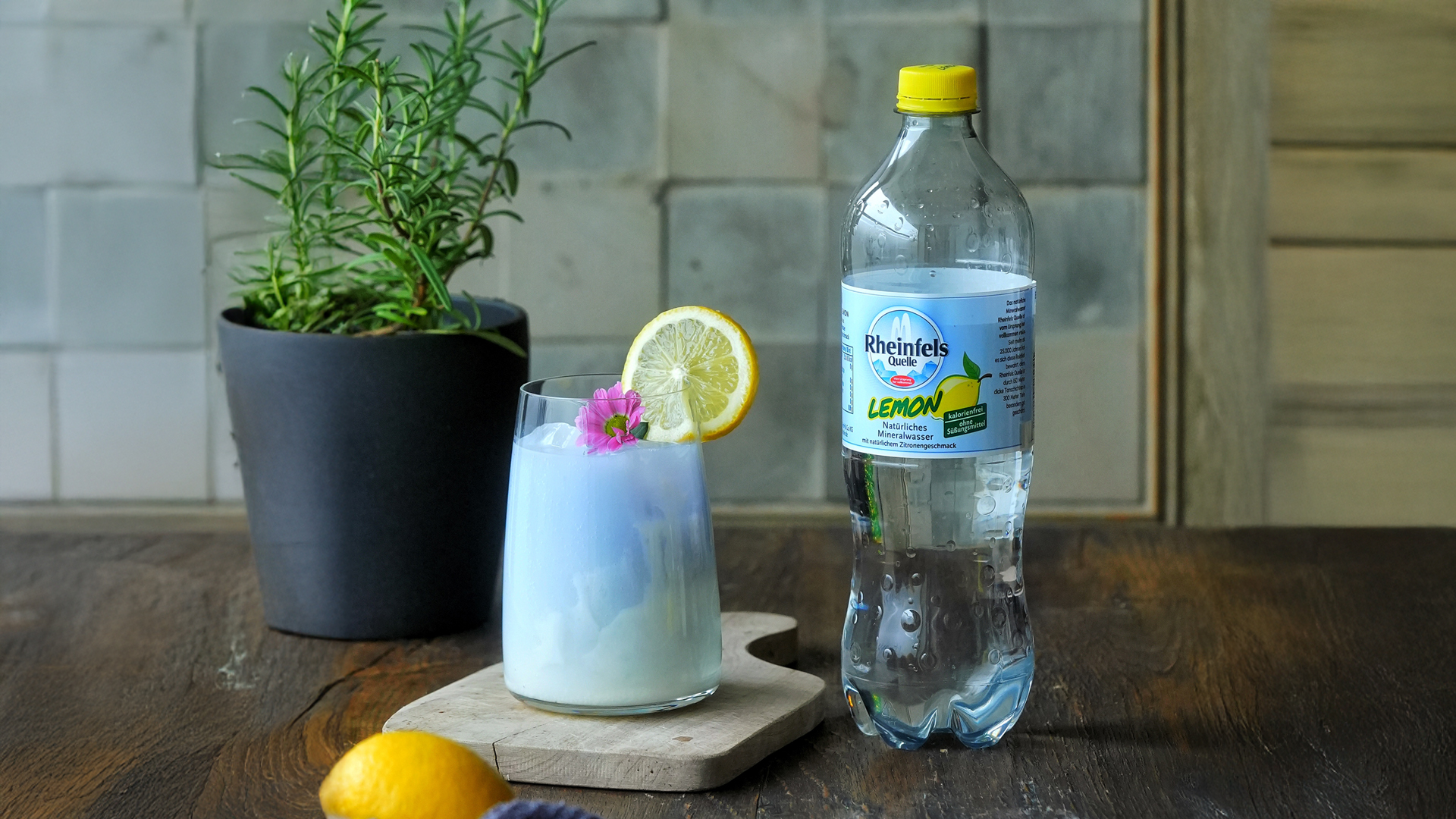 Schmetterlingsblütentee-Mocktail in einem Glas daneben steht ein Flasche Rheinfels Quelle Lemon.