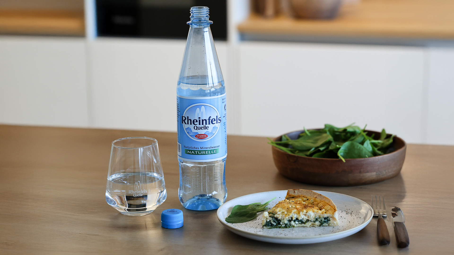 Tortilla-Quiche mit Spinat und Feta daneben steht ein Flasche Rheinfels Quelle Naturelle.