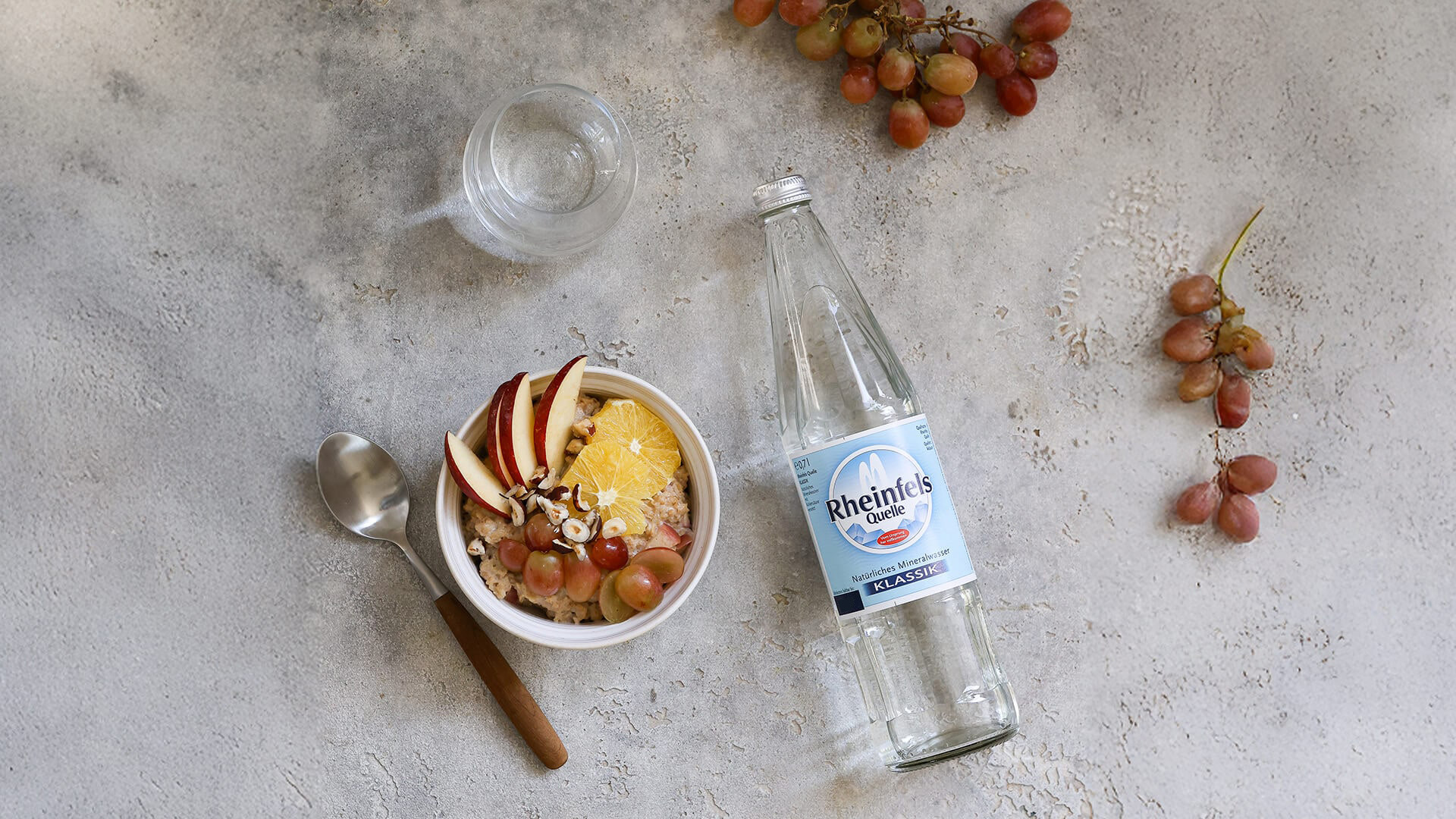 Eine Schüssel Porridge mit Früchten neben einer Flasche Rheinfels Quelle Klassik