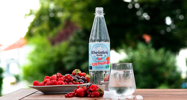 Rheinfels Rote Früchte Flasche auf dem Gartentisch, daneben ein Teller mit Beeren