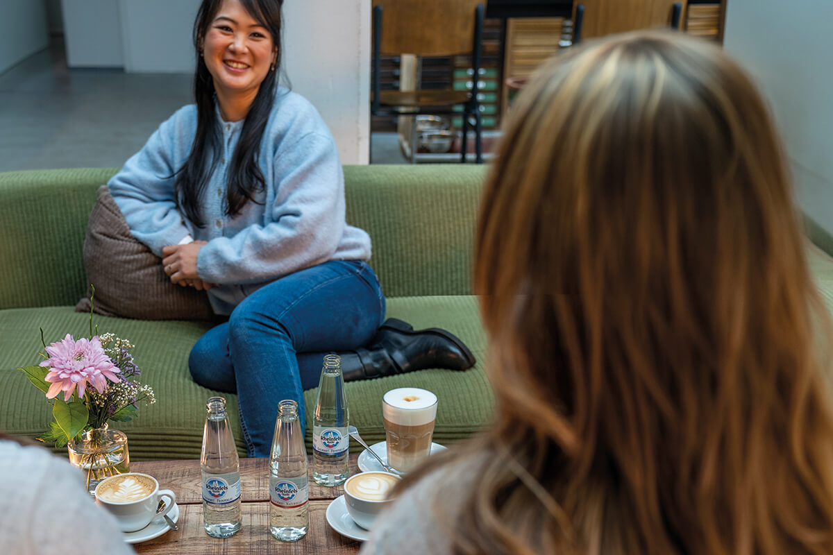 Mehrere Personen sitzen an einem Tisch mit Rheinfels Quelle Gastronomie Flaschen und Tassen mit Kaffee und einem Glas Latte Macchiato 